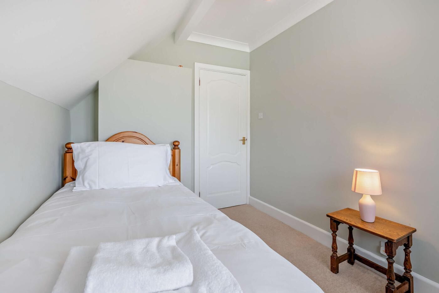A bedroom with a bed, a bedside table with a lamp, and a door.