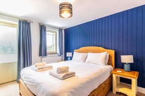 Une chambre à coucher avec un lit, une table de chevet, une lampe, une fenêtre avec des rideaux et un radiateur.