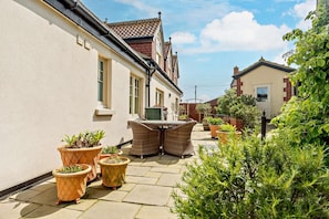 Une cour avec une table et des chaises de patio, entourée de plantes en pot et d’un petit jardin.