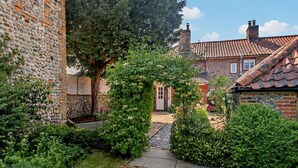 A stone wall with a garden path leading to a house with a tiled roof. - 2 Bed in Southrepps (oc-n27613) (Southrepps)