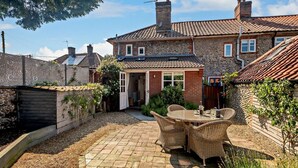 A brick house with a tiled roof, a garden with a patio table and chairs, and a wooden fence. - 2 Bed in Southrepps (oc-n27613) (Southrepps)