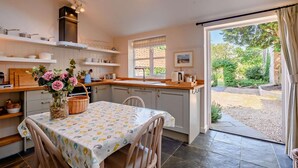 A cozy kitchen with a dining area, featuring a table with a floral tablecloth, a basket, and a vase of flowers. - 2 Bed in Southrepps (oc-n27613) (Southrepps)
