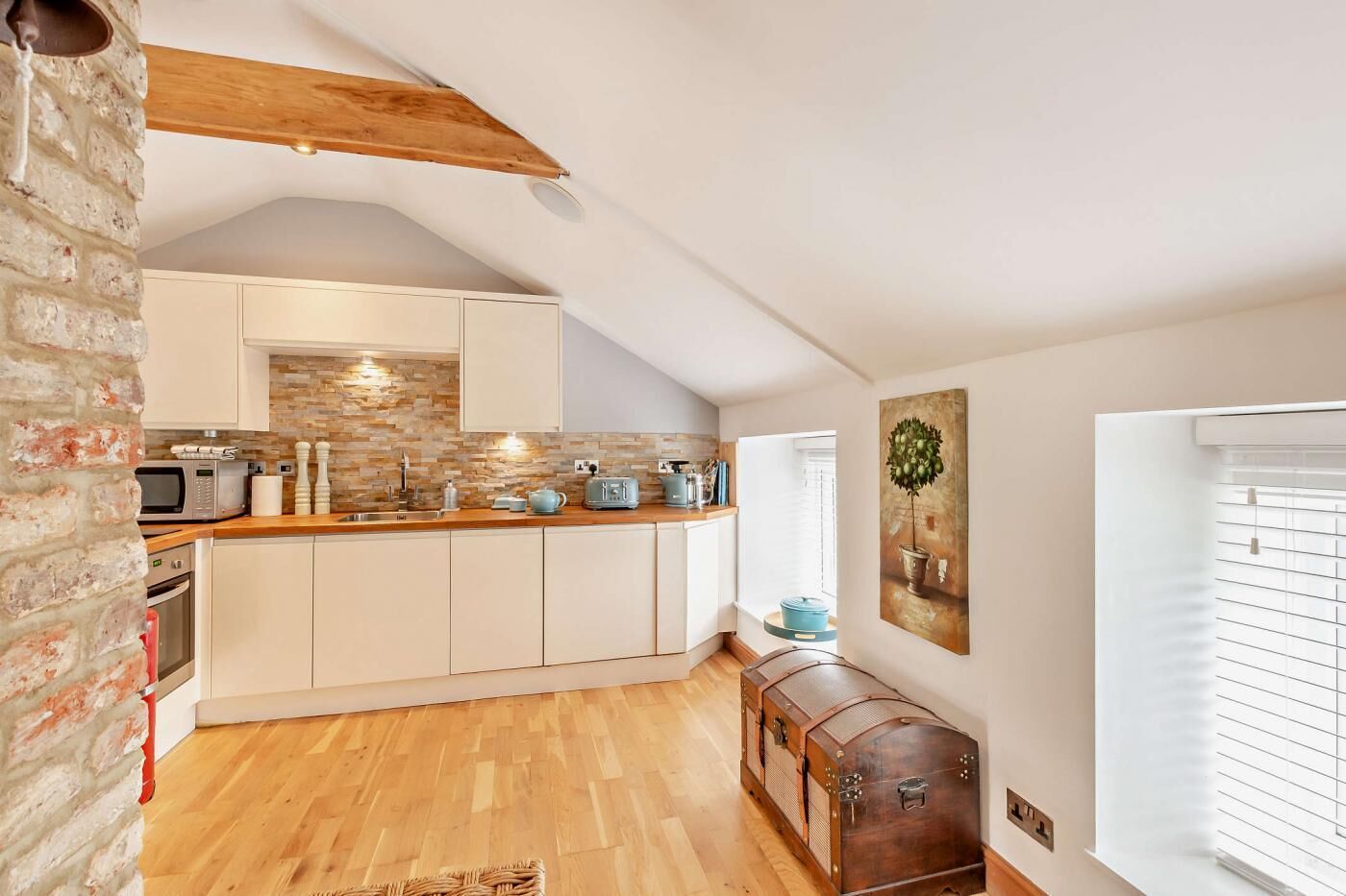 A modern kitchen with white cabinets, a wooden countertop, and a brick wall.