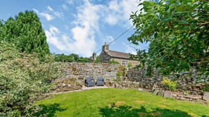 A stone wall with a grassy backyard, two chairs, and a building in the background.