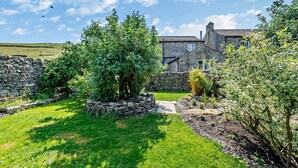 A stone wall, a garden with various plants, and a stone building with a chimney.