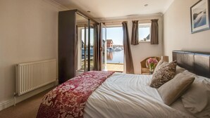 Een slaapkamer met een bed, een stoel, uitzicht op de jachthaven en een raam met gordijnen.