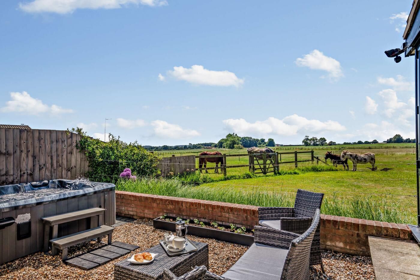 A patio with outdoor seating, a hot tub, and a view of a farm with horses.
