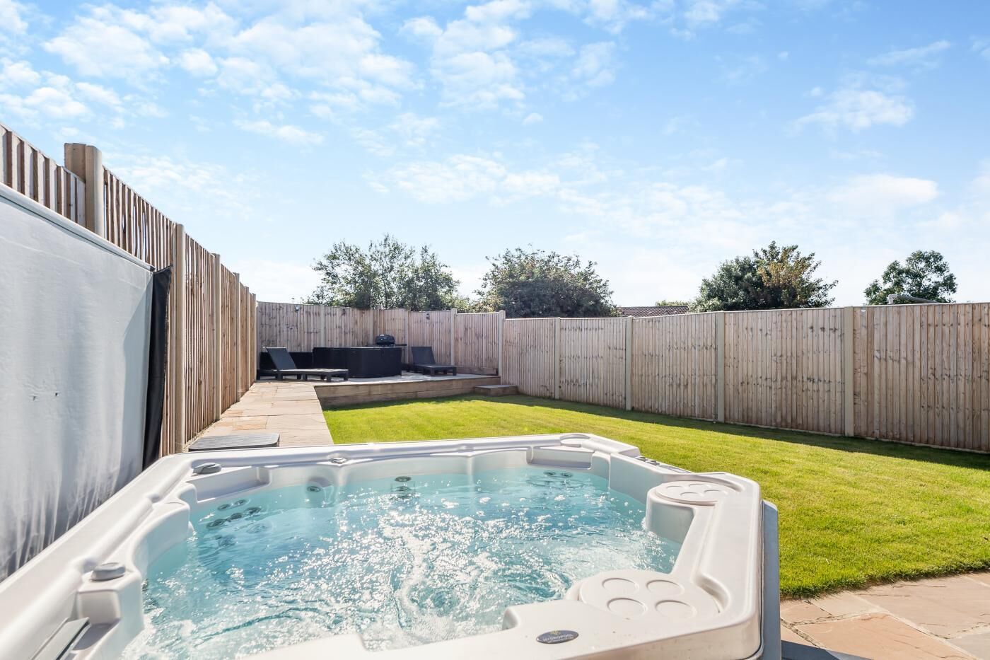 Een achtertuin met een jacuzzi, een houten schutting en een gazon.