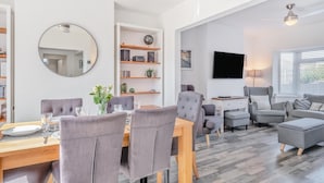 En moderne stue med spiseplads, grå polstrede møbler, et fladskærms-tv og en loftsvifte.
