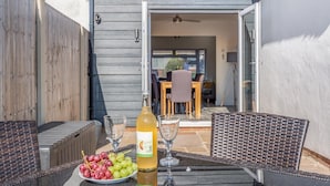 En patio med et bord dækket til to personer, med en vinflaske, en skål med druer og to glas.