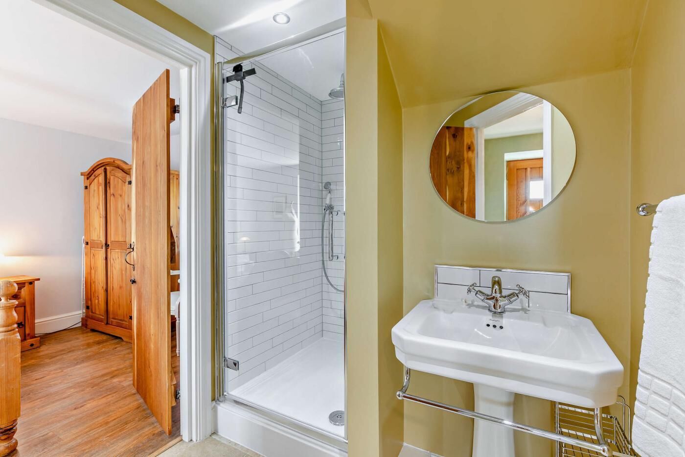 A bathroom with a shower, a sink, and a wooden wardrobe.