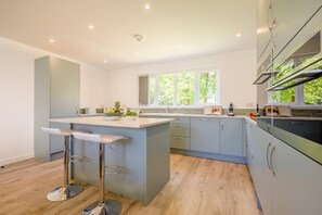 Une cuisine moderne dotée d’un îlot central, de tabourets de bar, d’une grande fenêtre et de meubles de rangement aux couleurs claires.