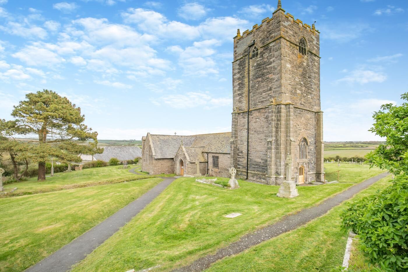 A church with a tall tower, a paved pathway, and a grassy area with trees.