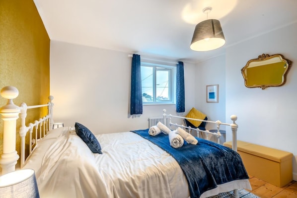 A bedroom with a bed, a window with curtains, a bedside table, a lamp, a bench, and a mirror on the wall. - 3 Bed in Kessingland (oc-b27635) (Kessingland)