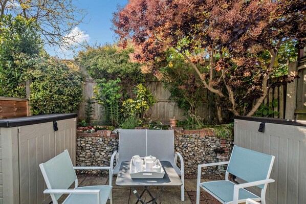 An outdoor patio area with a table and two chairs, surrounded by a stone wall and a wooden fence. - 3 Bed in Kessingland (oc-b27635) (Kessingland)