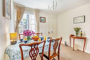 A dining room with a table set for breakfast, a chandelier, and a window with curtains.