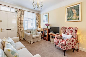 A living room with a sofa, armchair, TV, and a painting on the wall.