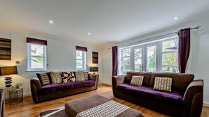 Un soggiorno moderno con due divani, un tavolino da caffè e un camino. Sono presenti ampie finestre con tende, e il pavimento è in legno.