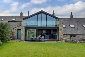 A modern house with a large glass extension, stone walls, and a well-maintained lawn. - 4 Bed in Beadnell (oc-b27650) (Beadnell)