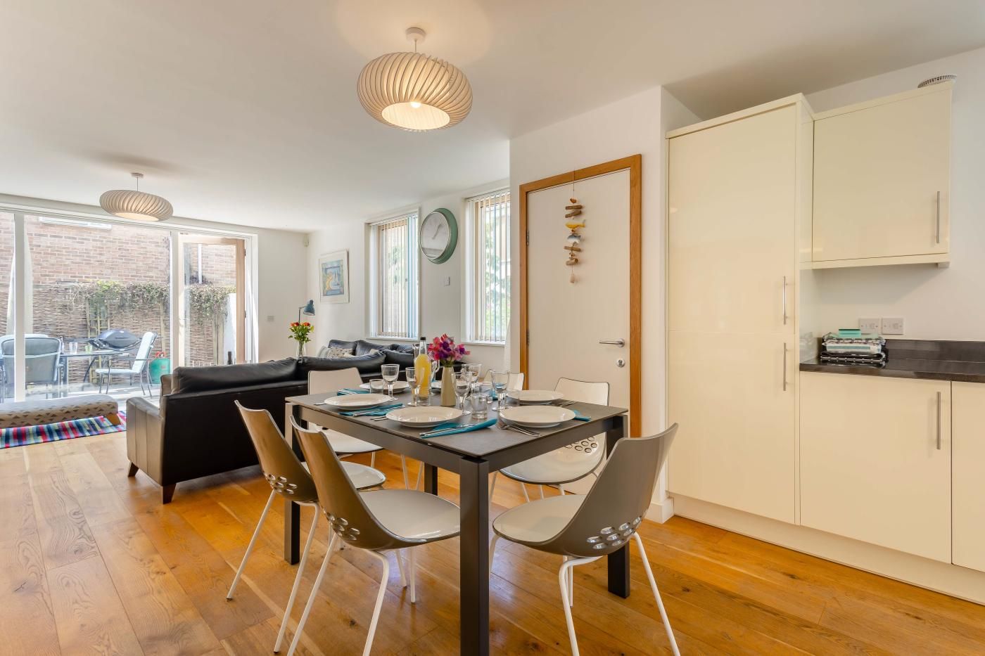 A modern kitchen with a dining area, wooden flooring, and a view to the outside.