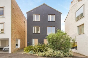 A modern two-story residential building with a dark facade, multiple windows, and a small garden area with various plants. - 2 Bed in Southwold (oc-ftw2) (Southwold)