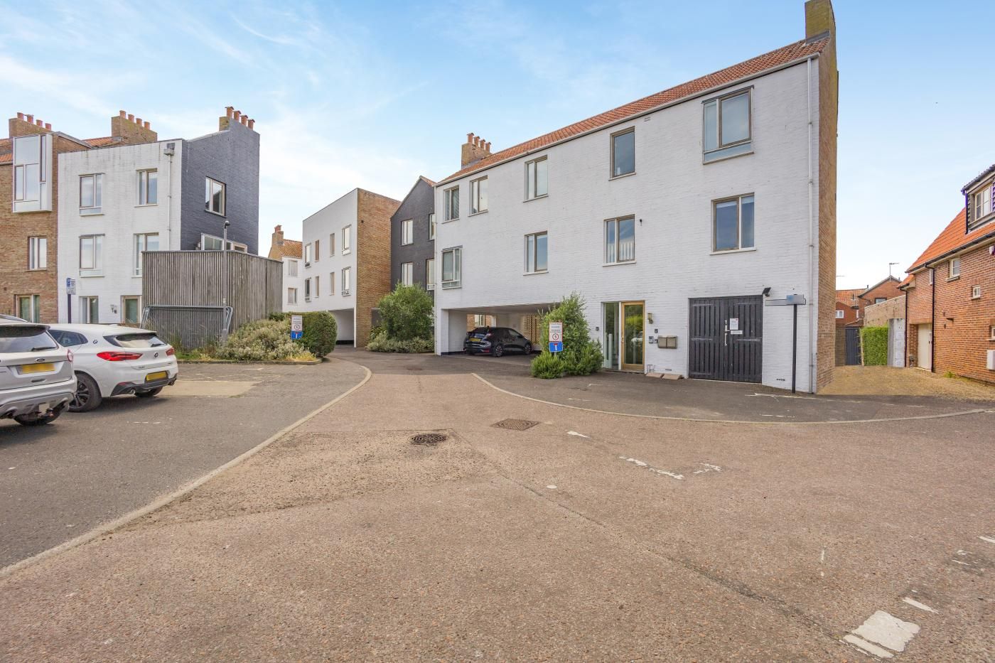 A residential street with multi-story houses, a parking area, and a gated entrance.