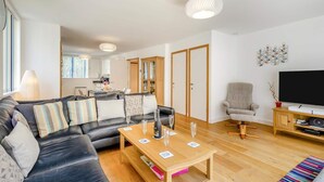 A modern living room with a sofa, a coffee table, a TV, and a dining area. - 2 Bed in Southwold (oc-ftw2) (Southwold)