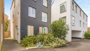 A residential building with a dark brick facade, white exterior walls, and a small garden area with various plants. - 2 Bed in Southwold (oc-ftw2) (Southwold)