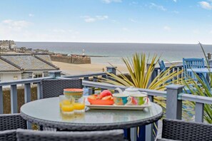 Eine Terrasse direkt am Meer mit einem gedecktem Frühstückstisch, mit Blick auf den Ozean und ein Küstendorf.