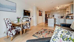 Een moderne woonkamer met een eethoek, een keuken en een aan de muur bevestigde televisie.