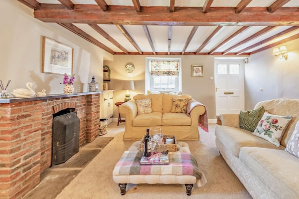 A cozy living room with a fireplace, a sofa, a coffee table, and a window with floral curtains.