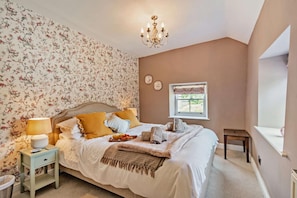 A bedroom with a bed, bedside lamps, a window, and a chandelier.