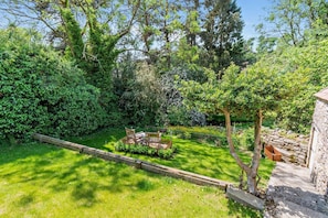 Ein Garten mit einer Holzterrasse, einer Steinmauer und verschiedenen Bäumen und Sträuchern.