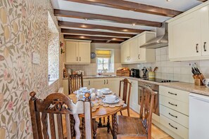 Eine Küche mit Holzkstühlen, einem Esstisch für vier Personen und einem Fenster mit Jalousien.