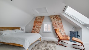 Une chambre avec un plafond en pente, un lit, une chaise, un petit radiateur et une fenêtre.