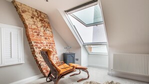 Une pièce avec un plafond en pente, un mur en briques, un fauteuil à bascule, un tapis en fourrure et un radiateur.
