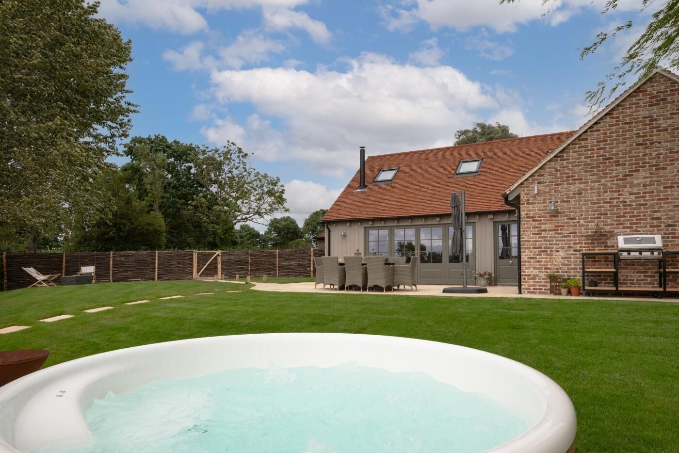 Een achtertuin met een zwembad, een stenen huis en een terras met tuinmeubilair.