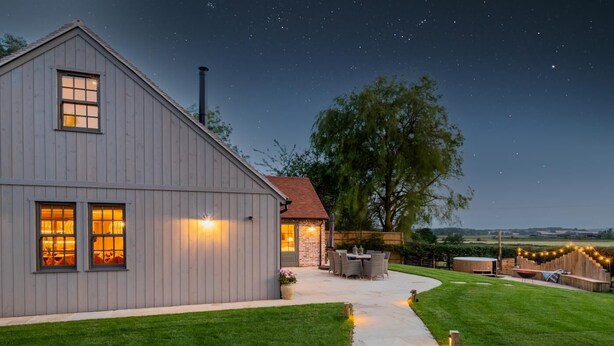 A modern house with a large garage, a patio with outdoor furniture, and a well-maintained lawn. - 3 Bed in Wittersham (oc-m27683) (Wittersham)