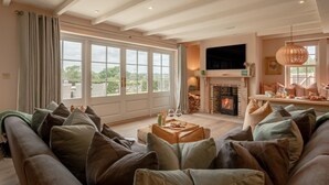 A spacious living room with a large sofa, a fireplace, and a dining area with a view of the outdoors. - 3 Bed in Wittersham (oc-m27683) (Wittersham)