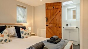 A bedroom with a bed, a wooden door, a bathroom with a sink, and a window with blinds. - 3 Bed in Wiveton (oc-d19479) (Wiveton)
