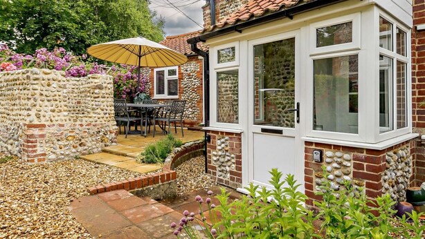A house with a stone wall, a patio with a table and chairs, and a door with windows. - 3 Bed in Wiveton (oc-d19479) (Wiveton)