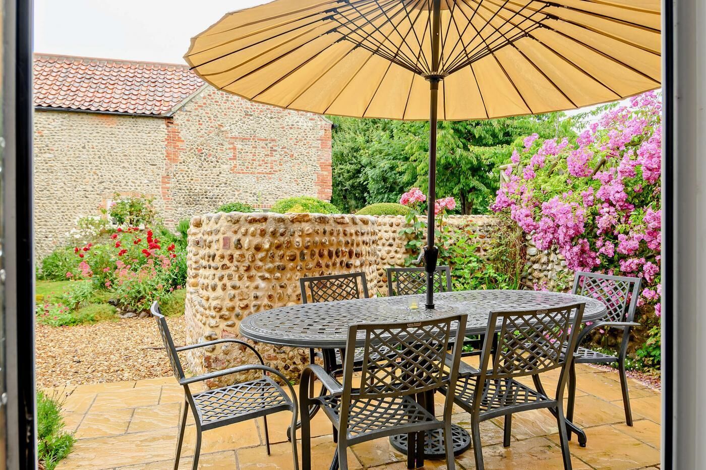 An outdoor patio with a round table and chairs, a large umbrella, and a stone wall with a textured surface.