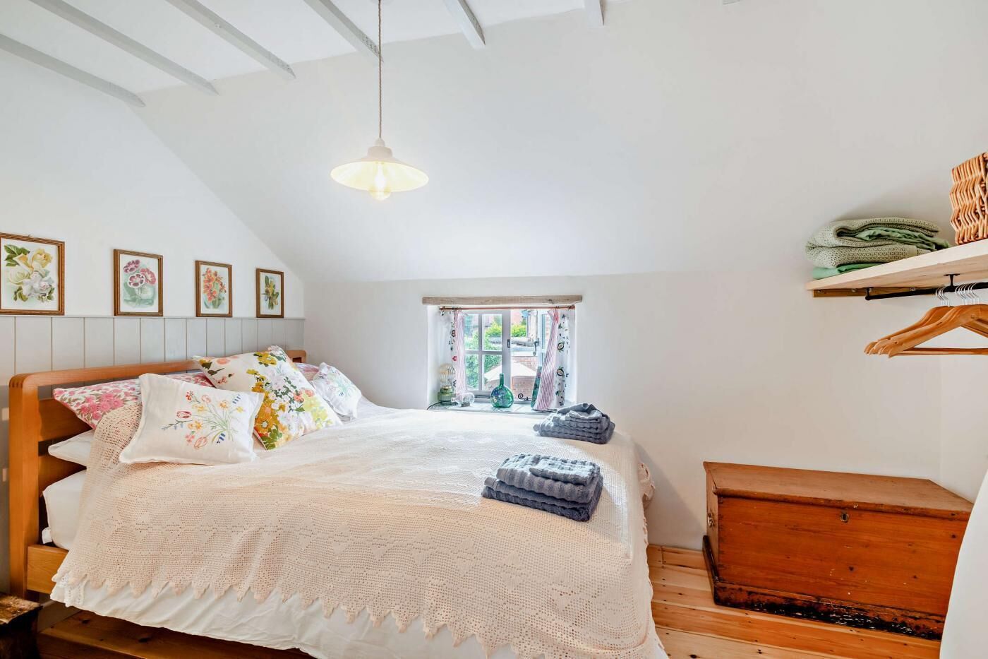 Un dormitorio acogedor con una cama de madera, un ventanal con cortinas, una lámpara colgante y un aparador de madera.