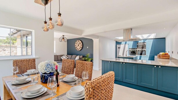 A modern kitchen with blue cabinets, a dining area with wicker chairs, and a large window. - 3 Bed in Tholthorpe (oc-r23426) (Tholthorpe)