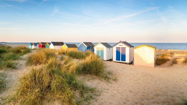 Eine Reihe von Strandhütten mit einem Sandstrand und Dünen im Vordergrund.
