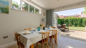 Ein Essbereich mit einem Tisch für vier Personen, einem Fenster mit Blick auf einen Garten und einem Gemälde an der Wand.