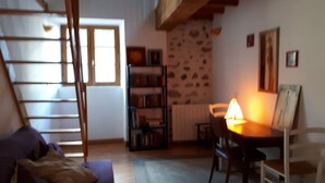 Ett mysigt vardagsrum med en trätrappa, en bokhylla, ett matbord med en lampa och en tavla på väggen.