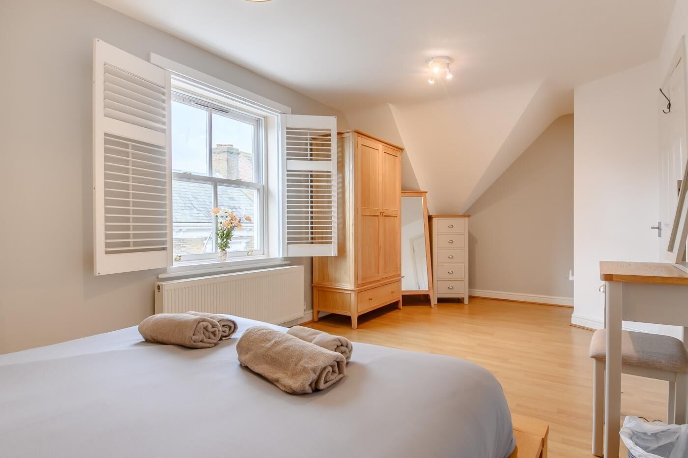 Ein Schlafzimmer mit einem großen Bett, einem Holzschrank, einem Heizkörper und einem Fenster mit Jalousien.