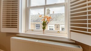 Een kamer met raam, witte luiken, een radiator en een bloevas.