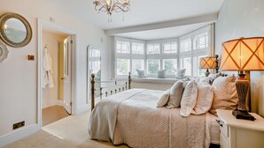 A bedroom with a large bed, a chandelier, a window seat, and a lamp. - 5 Bed in West Runton (oc-f27744) (West Runton)